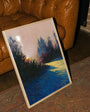 Painting of a sunset over water on a wooden easel against a brown leather couch and brick wall.